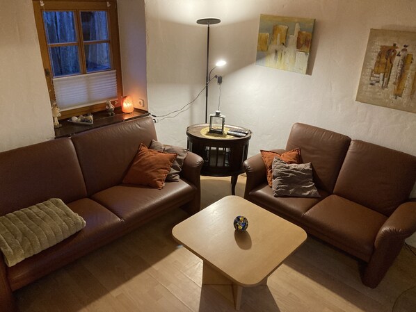 Un salon avec deux canapés en cuir marron, une table basse en bois et une petite table d’appoint sur laquelle est posée une lanterne.