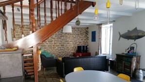 Een gezellige zithoek met een stenen muur, een houten trap, een eettafel met gele stoelen en een visdecoratie aan de muur.