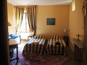 Une pièce avec deux lits, une table, une chaise, une lampe et un tableau au mur.