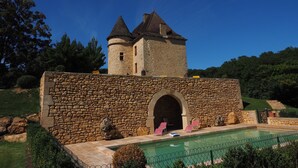 Un edificio de piedra con una torre, piscina y un muro de piedra.