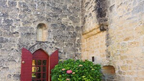 Un edificio de piedra con puerta roja y un pequeño jardín lleno de flores rosadas.