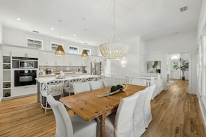 A modern kitchen with white cabinetry, a wooden dining table, and pendant lighting. - PRIVATE BEACH/POOL ACCESS -Minutes to the beach- Charming-4 Bikes Included (Rosemary Beach)