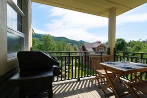 Un balcon doté d’un barbecue, d’une table à manger et de chaises, offrant une vue panoramique sur un paysage pittoresque avec des maisons et des montagnes.