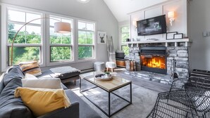 Ein modernes Wohnzimmer mit Kamin, großen Fenstern und einem Fernseher.
