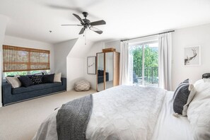 Une chambre à coucher comprenant un lit, un ventilateur de plafond, une fenêtre avec des rideaux, un canapé et un miroir.