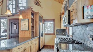 Une cuisine dotée de meubles en bois, de plans de travail en granit, d’un pare-feu en pierre et d’une grande fenêtre.