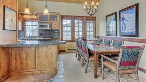 Une cuisine avec des meubles en bois, un plan de travail en granit et un coin repas comprenant une table et des chaises en bois.