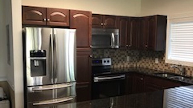 A kitchen with a stainless steel refrigerator, microwave, and oven, a granite countertop, and wooden cabinets. - A small piece of South Carolina Heaven (Myrtle Beach)