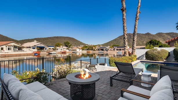 A patio with outdoor seating, a fire pit, and a view of a lake and mountains.