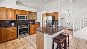 A modern kitchen with wooden cabinets, stainless steel appliances, and a central island with stools.