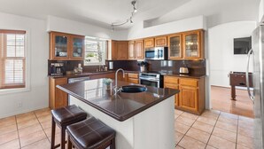 A modern kitchen with wooden cabinets, a central island with a sink, stainless steel appliances, and a bar stool.