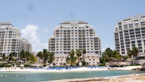 Een strandhotel met meerdere hoge gebouwen, een zandstrand en een zwembadgedeelte met ligbedden.