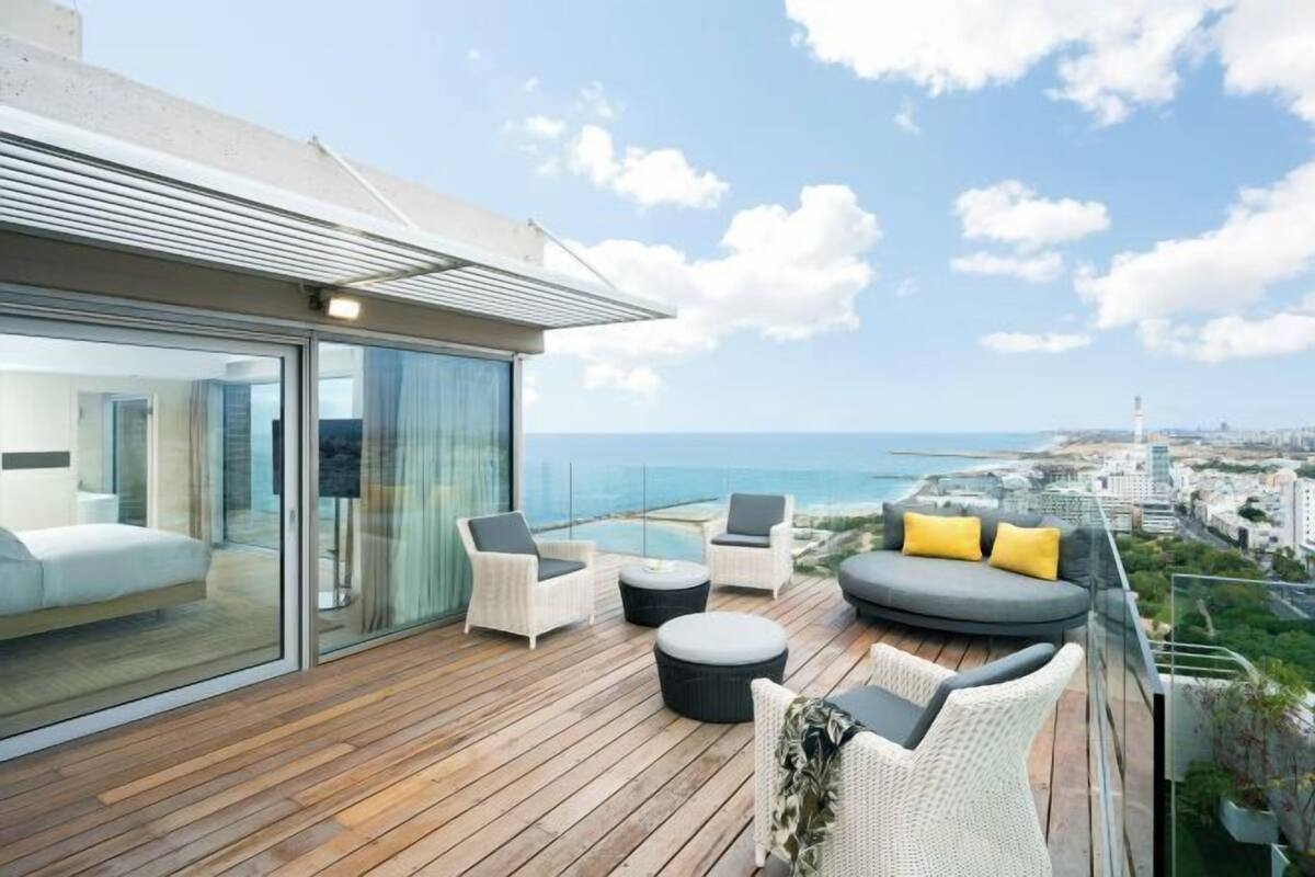 Een modern balkon met een houten vloer, glazen deuren en een zithoek met kussens.