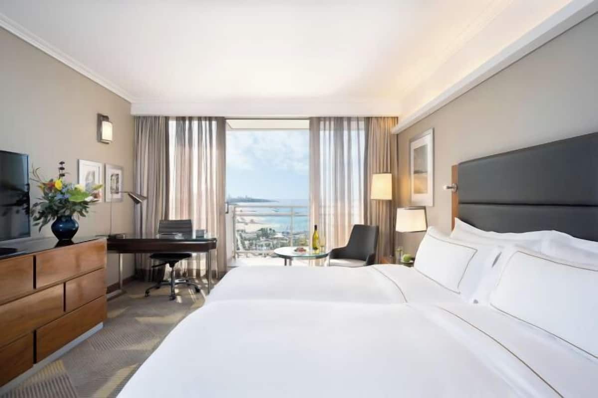 Een hotelkamer met een bed, bureau, stoel, televisie en uitzicht op de stad.