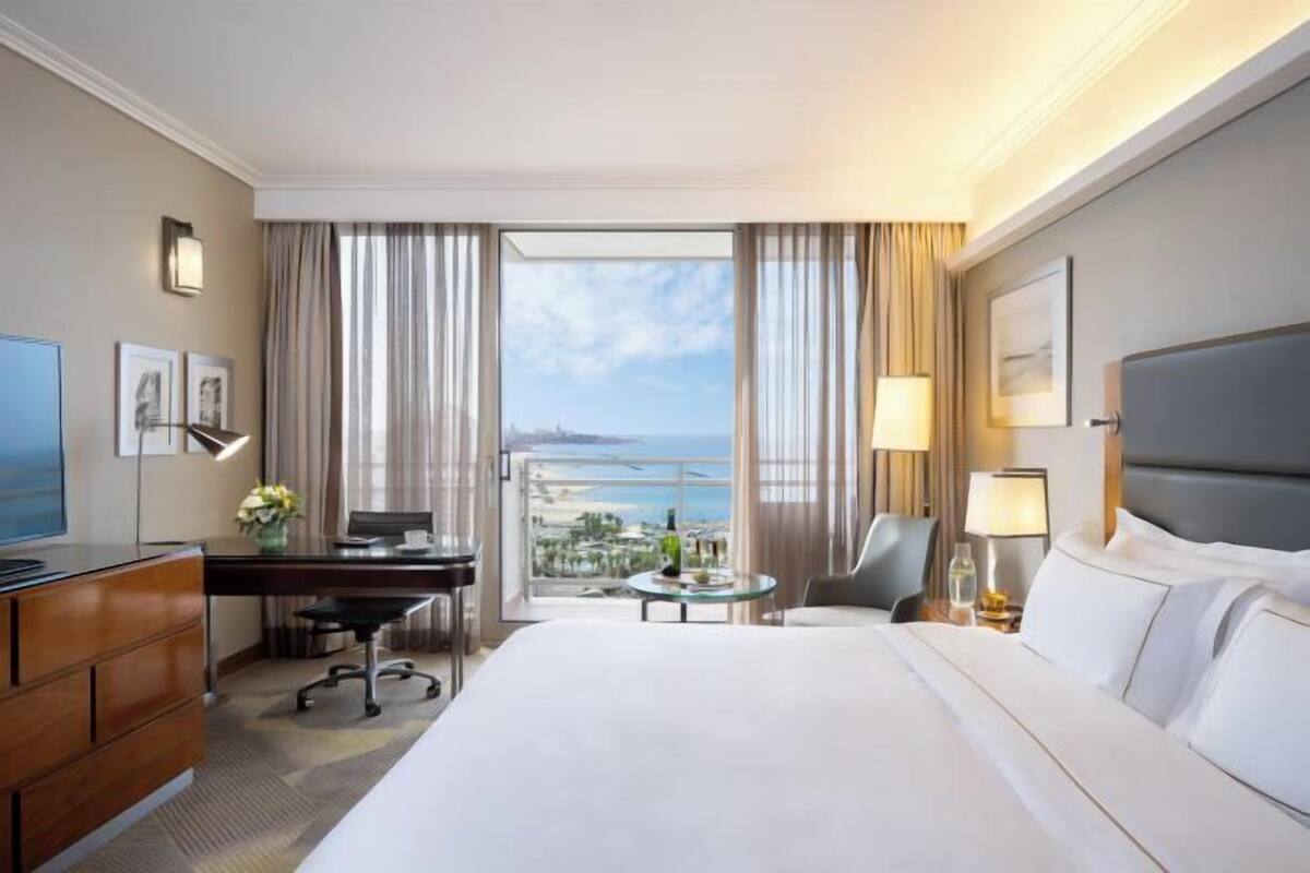 Een hotelkamer met een bed, bureau, stoel en een groot raam met uitzicht.