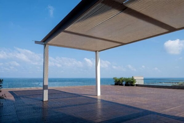 Una terraza abierta con vista al mar, que cuenta con una zona de estar cubierta y suelo de ladrillo.