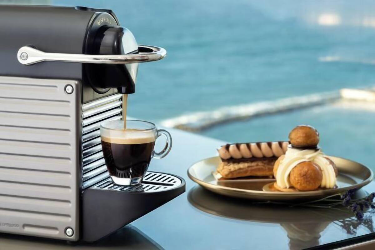 Een koffieapparaat op een tafel met een kop koffie en gebak.