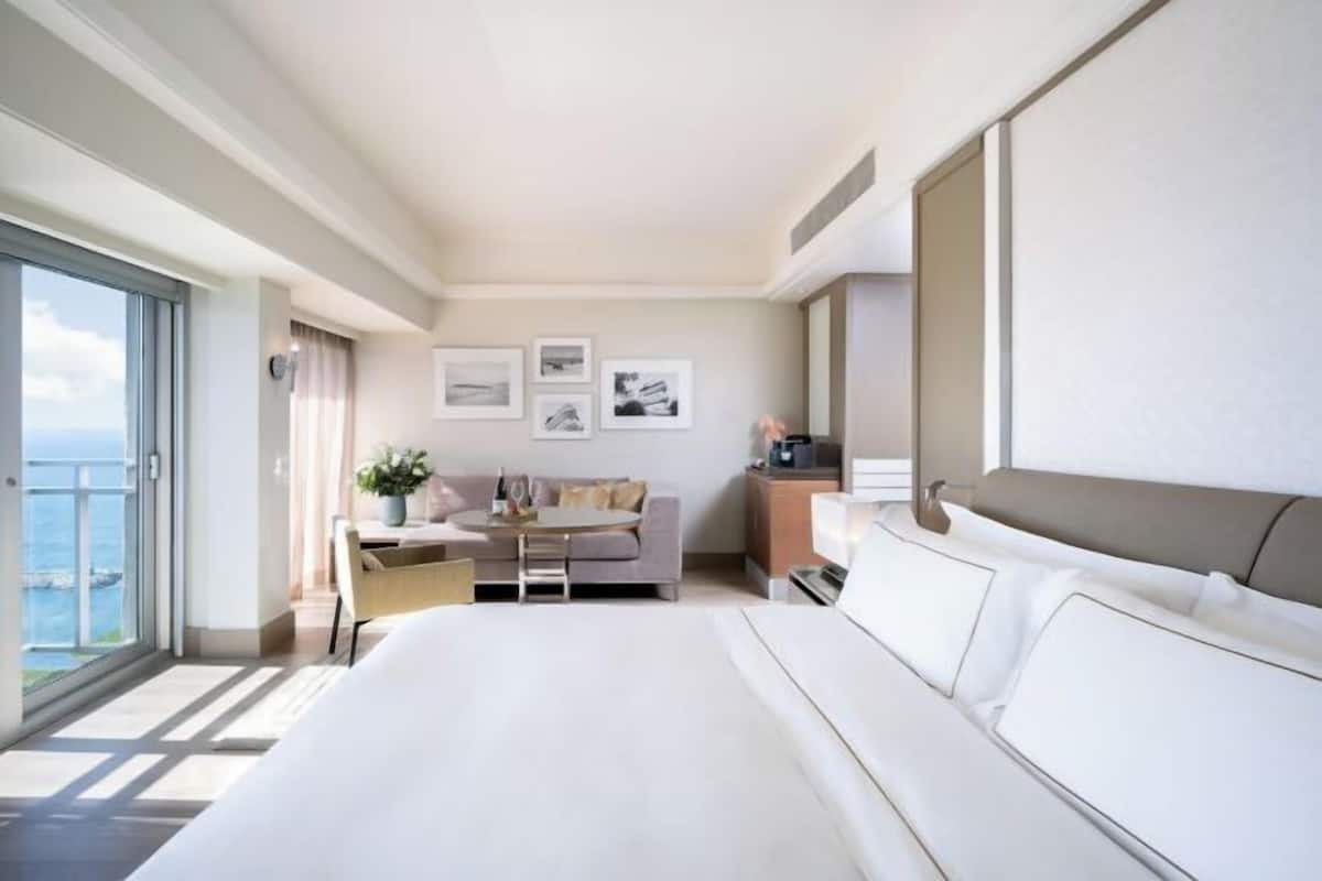 Een moderne hotelkamer met een groot bed, een bank, een eettafel en uitzicht op zee.