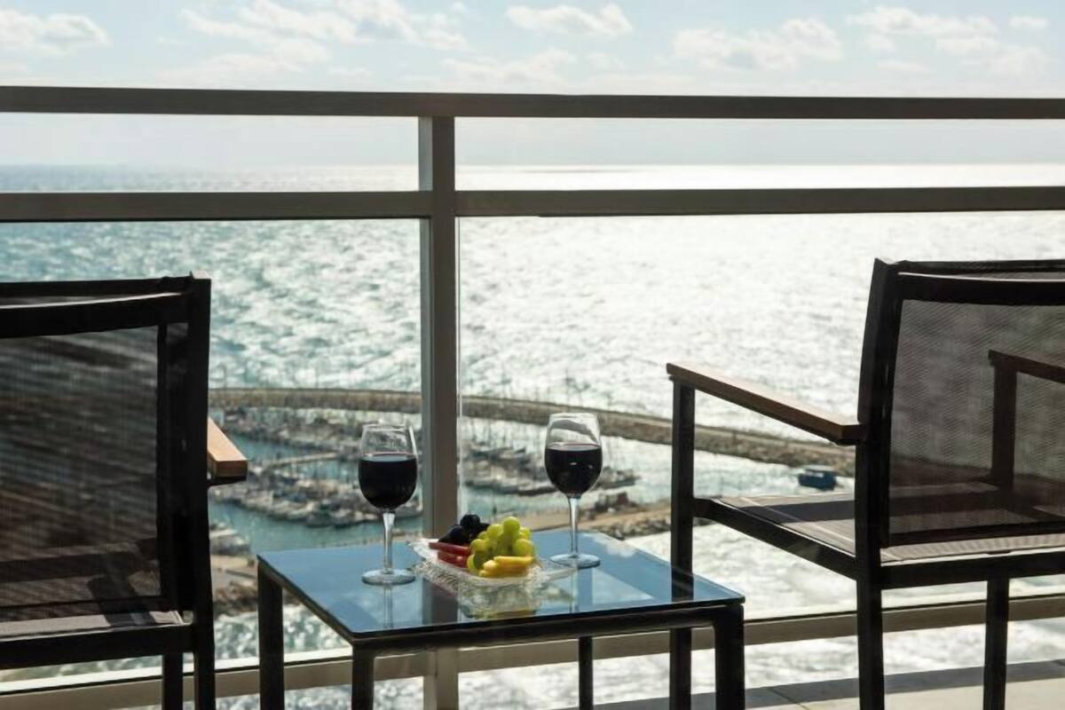 Een balkon met een tafel voor twee personen, twee glazen rode wijn en een schaal fruit.