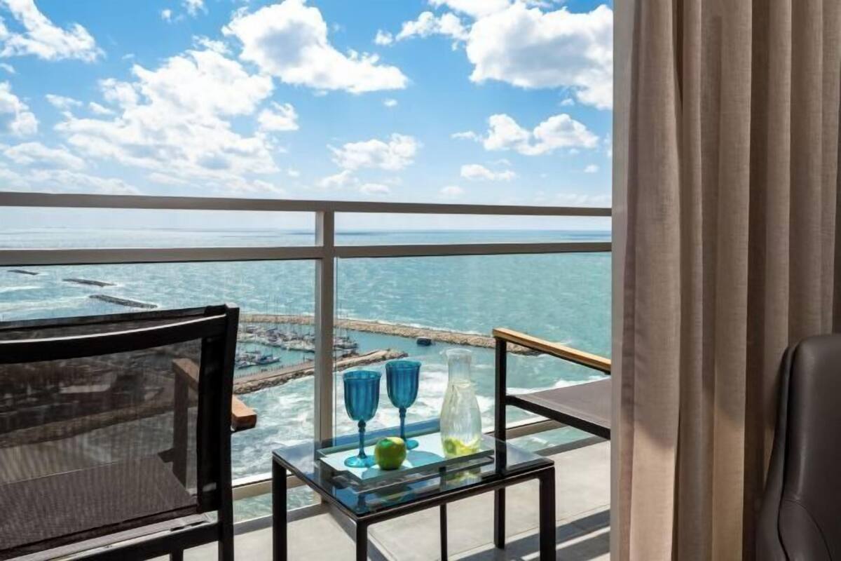 Een balkon met een glazen tafel, een stoel en uitzicht op zee.