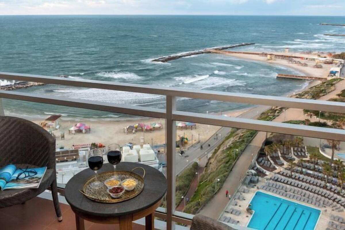 Een balkon met uitzicht op zee, een zwembad en een eettafel met glazen en eten.