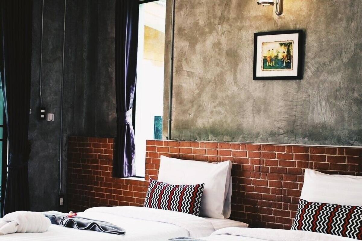 A hotel room with two beds, a brick accent wall, a framed picture, and a window with curtains.