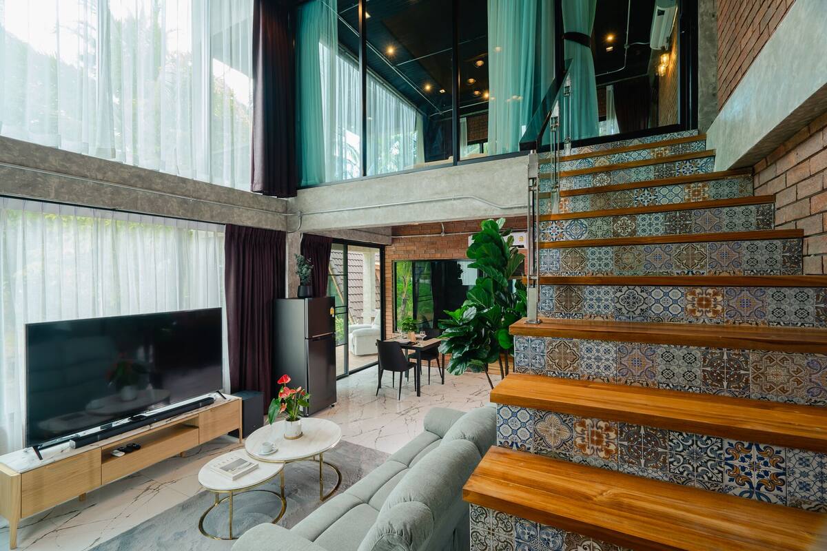 A spacious living area with a large flat-screen TV, a sofa, a coffee table, and a dining area with a table and chairs.
