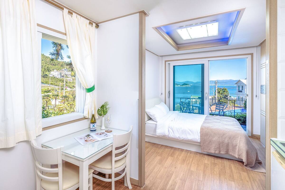 Quarto moderno com cama, escrivaninha e vista para o mar.