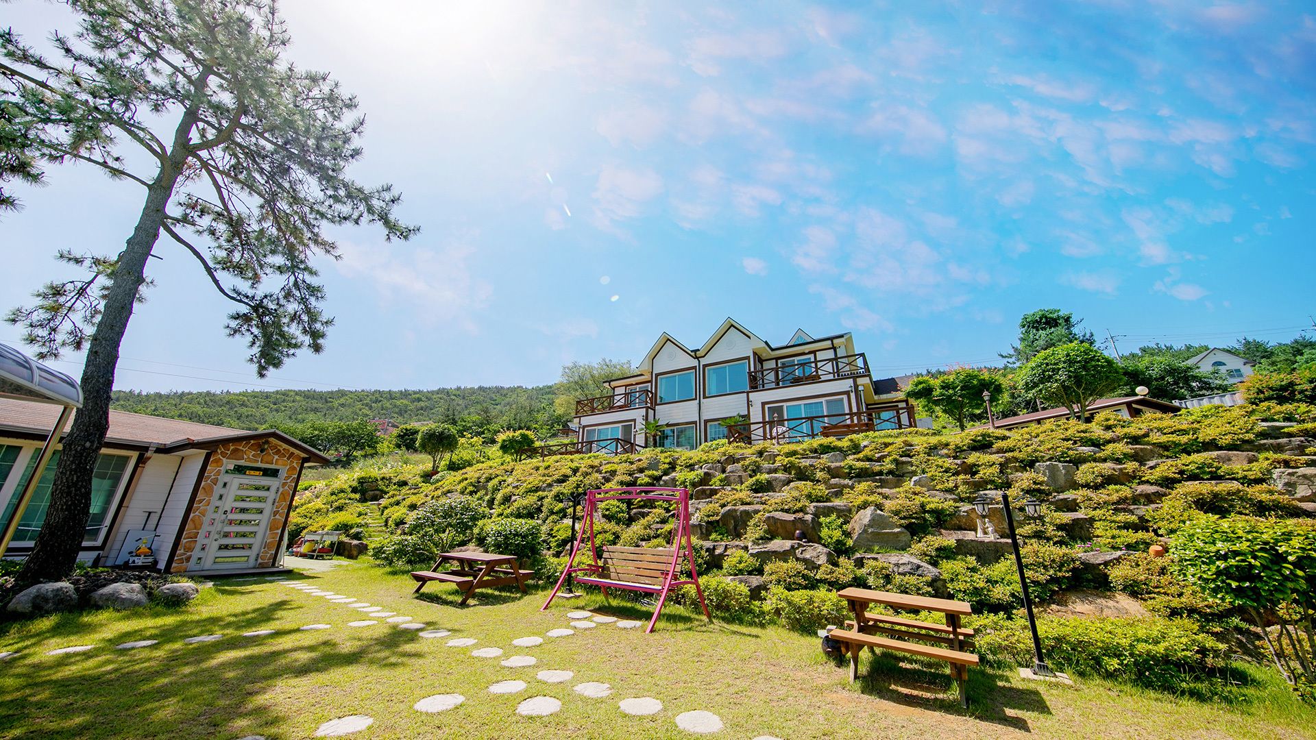 A two-story building with a modern design, surrounded by lush greenery and a stone pathway.