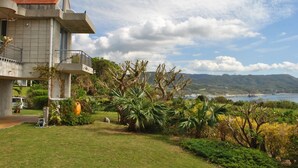 Une maison moderne dotée d’un balcon donnant sur un jardin luxuriant et offrant une vue panoramique sur la mer et les montagnes.