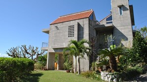 Un bâtiment moderne à l’extérieur en béton, avec un toit recouvert de tuiles rouges et une petite structure en forme de tour.