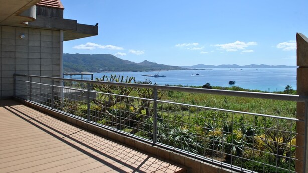 Un balcon offrant une vue sur un plan d’eau, des montagnes et un ciel dégagé.