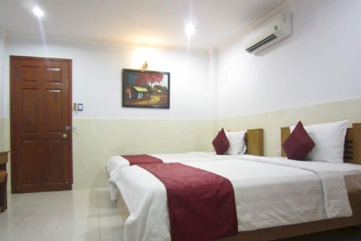 Una habitación de hotel con cama, puerta de madera, un cuadro en la pared y un equipo de aire acondicionado.