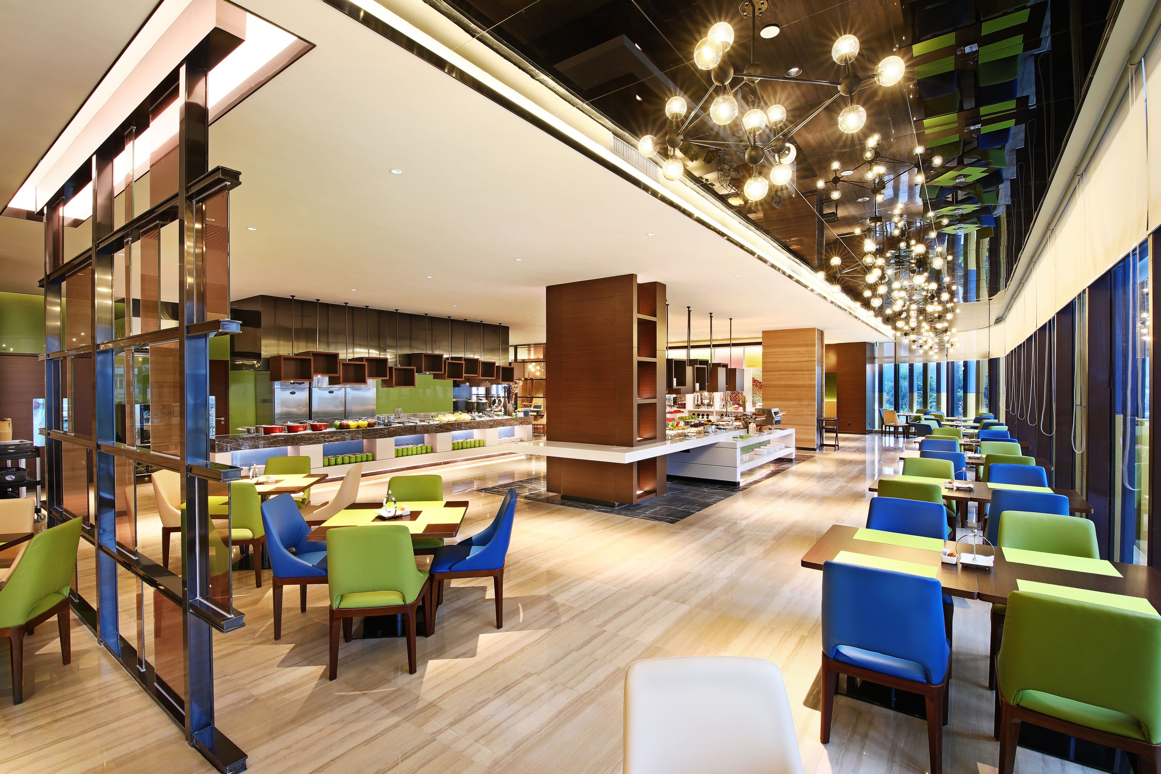 A modern hotel lobby with a central bar area, multiple seating arrangements, and a high ceiling with hanging lights.