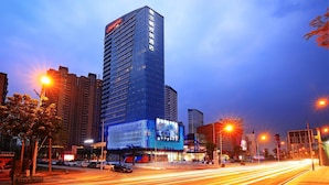 Un hotel moderno de gran altura, con un letrero llamativo, rodeado de otros edificios y calles concurridas.