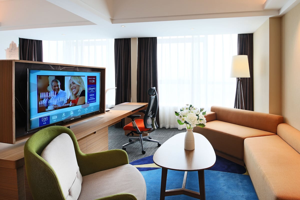 A hotel room with a TV, sofa, chairs, a small table, and a vase of flowers.