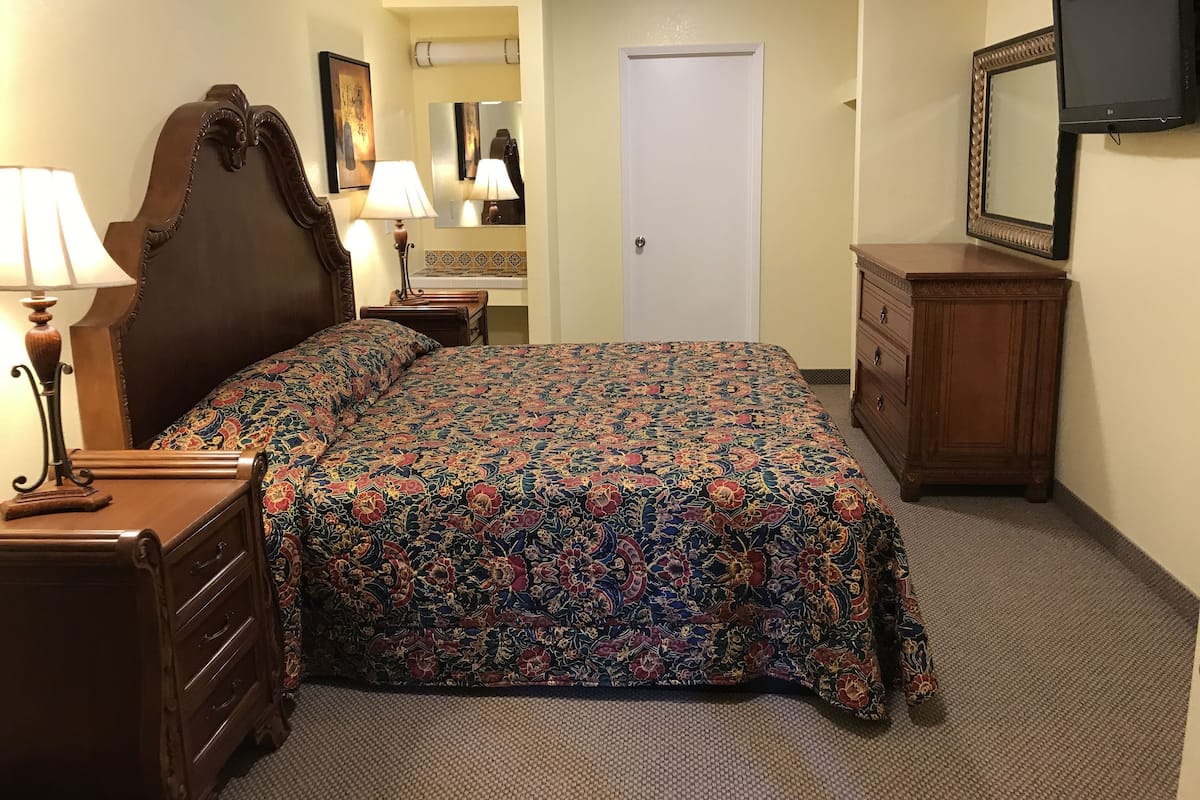 A hotel room with a bed, a dresser, a nightstand, a lamp, a mirror, and a television.