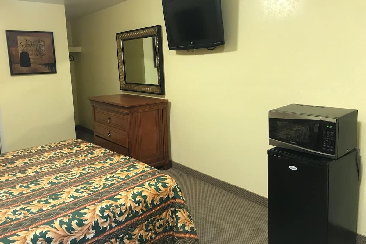 A hotel room with a bed, dresser, television, and microwave.