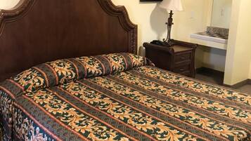 Un lit bien fait, avec une couvre-lit à motifs, une tête de lit en bois, une table de chevet avec une lampe et un petit miroir.