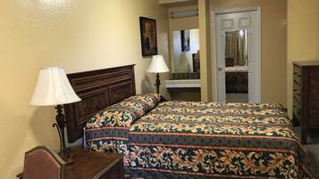 A bedroom with a bed, two bedside lamps, a dresser, a mirror, and a door leading to another room.