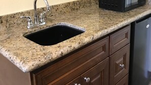 A kitchen with a granite countertop, a sink, a microwave, and wooden cabinets. - Hacienda Motel (Escondido)
