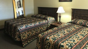 A hotel room with two beds, a nightstand, a lamp, a mirror, and a framed picture on the wall. - Hacienda Motel (Escondido)