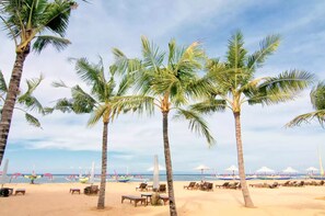 A beach with palm trees, lounge chairs, and umbrellas. - Suwardika Homestay and Dormitory - Hostel (Denpasar)