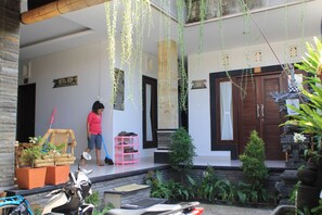 A covered outdoor area with a seating area, a door, and hanging plants. - Suwardika Homestay and Dormitory - Hostel (Denpasar)