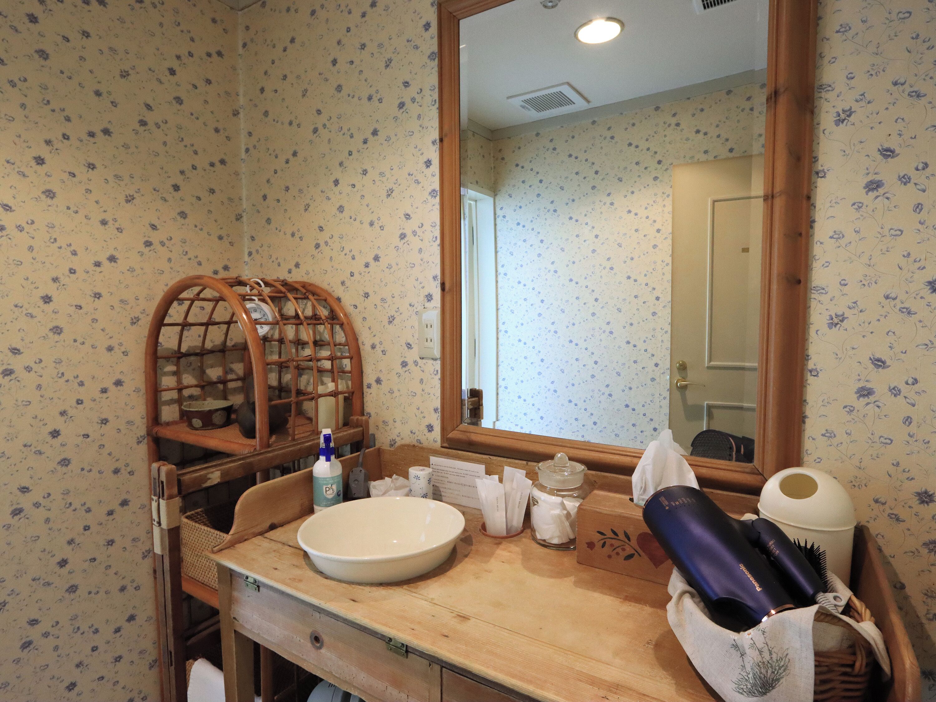 A bathroom with a wooden vanity, a large mirror, and a floral patterned wall.