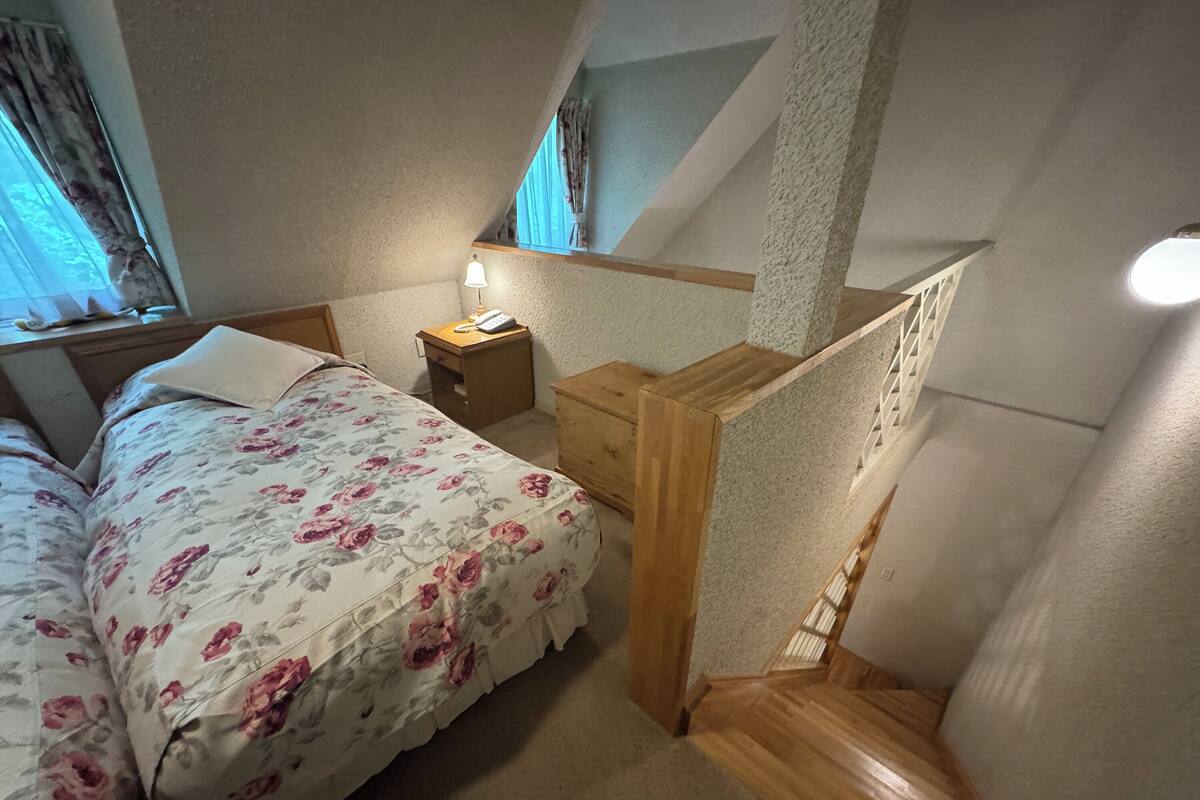 Ein Schlafzimmer mit Bett, Nachttisch, Lampe und einer Holztreppe.