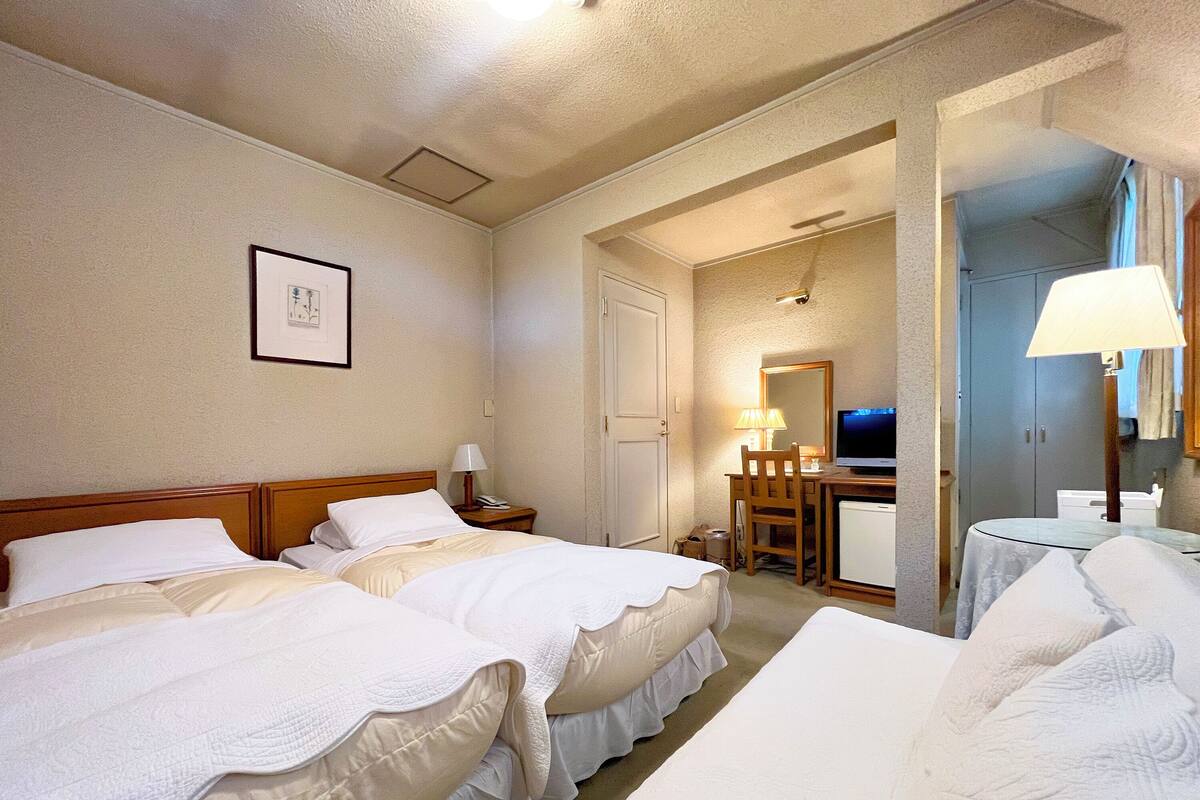Ein Hotelzimmer mit zwei Betten, einem Schreibtisch, einem Stuhl, einem Fernseher und einem Spiegel.