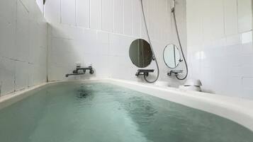 A modern bathroom with a freestanding bathtub, two wall-mounted mirrors, and a handheld showerhead.