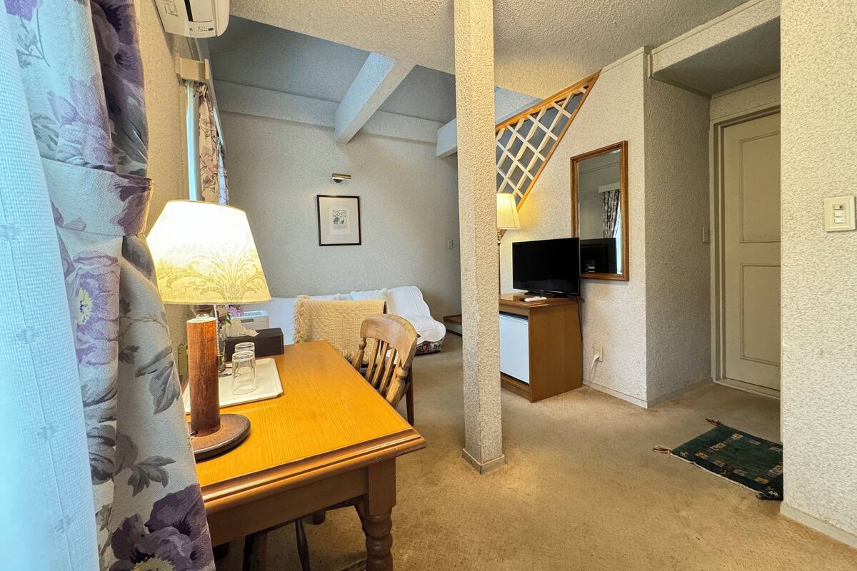 Ein gemütliches Zimmer mit einem Holztisch, einem Stuhl, einem Fernseher und einer Treppe, die in einen anderen Raum führt.