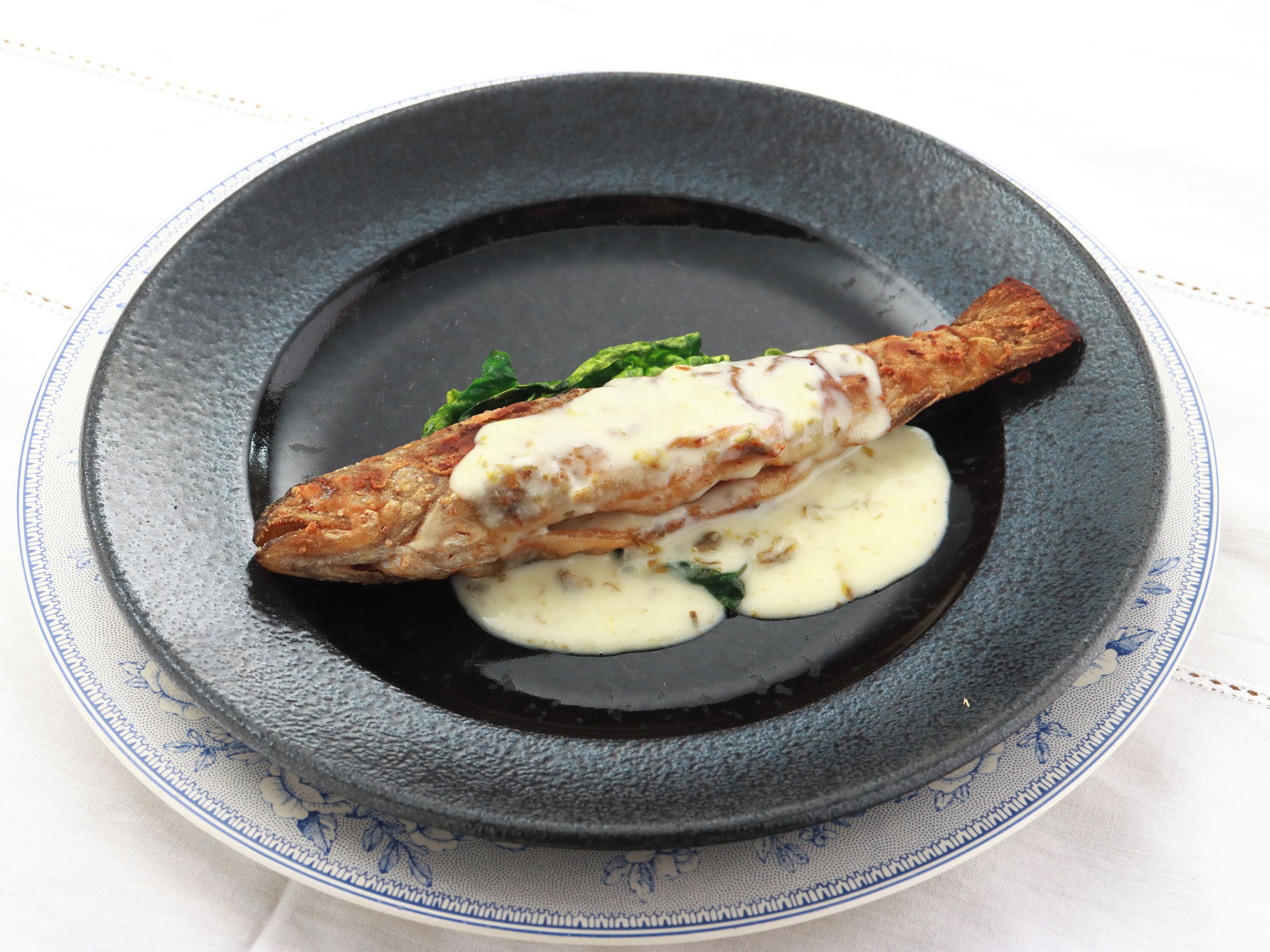 A plate with a fish, sauce, and greens.